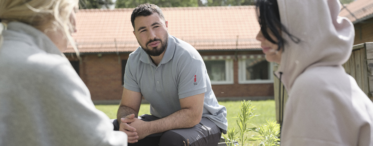 En medarbetare som sitter utomhus och pratar med två flickor.